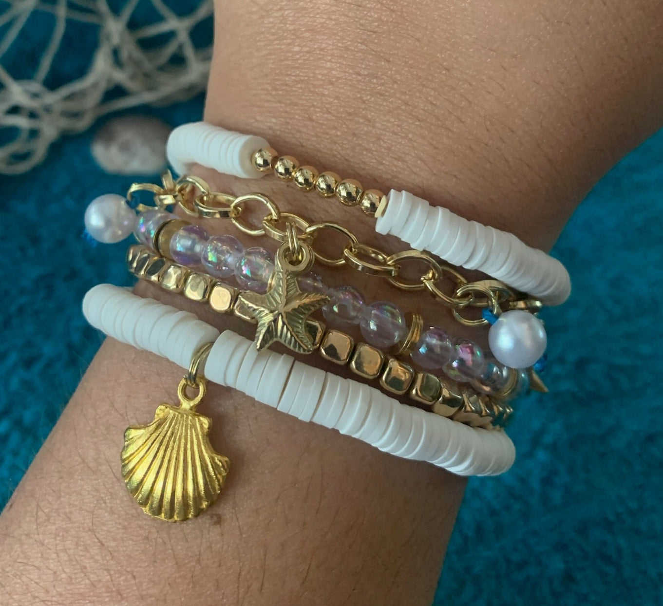 Stack of gold and white bracelets on a wrist with a blue textured background