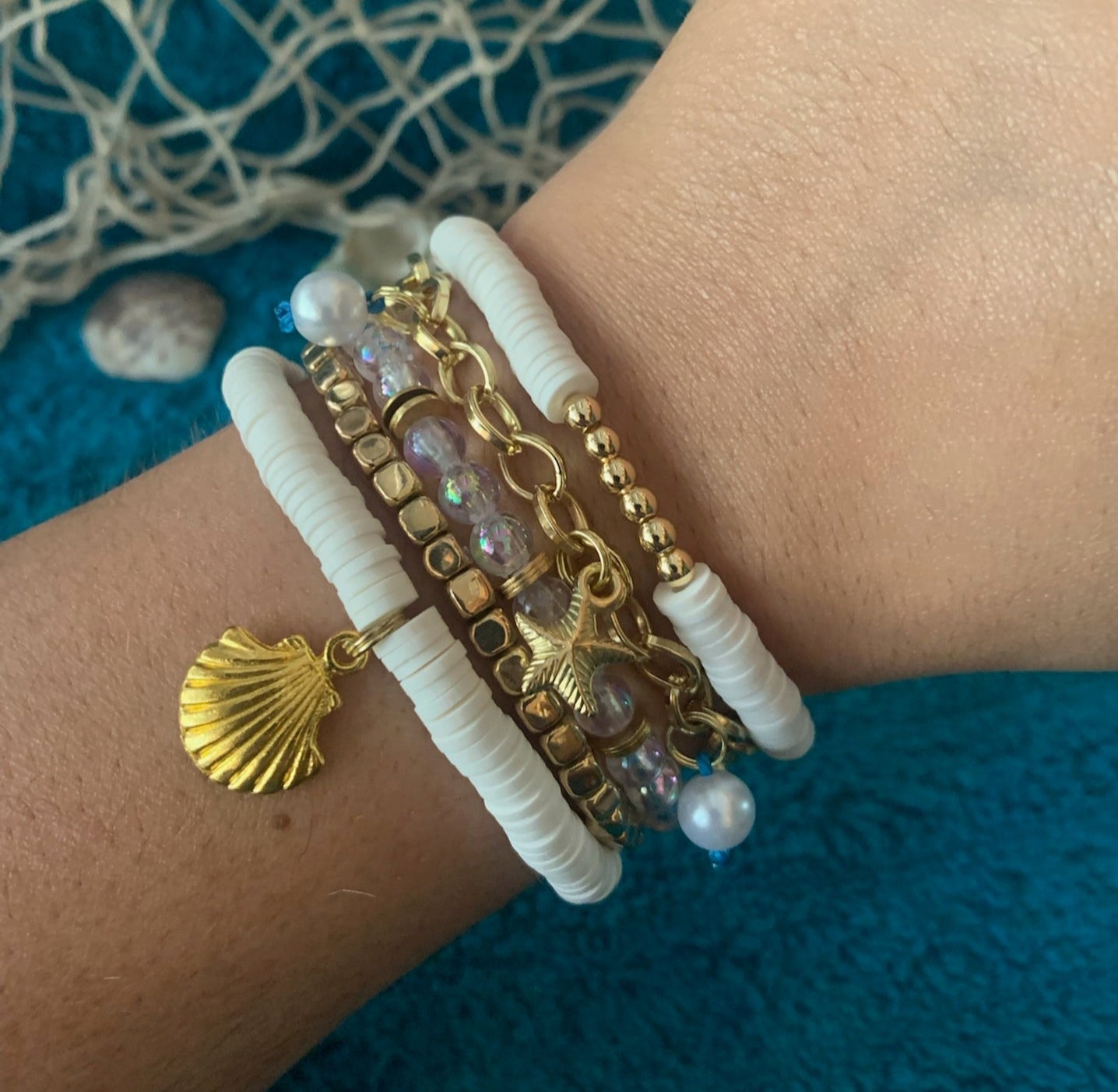 Close-up of a wrist wearing a decorative bracelet with gold elements and pearls on a textured blue background.