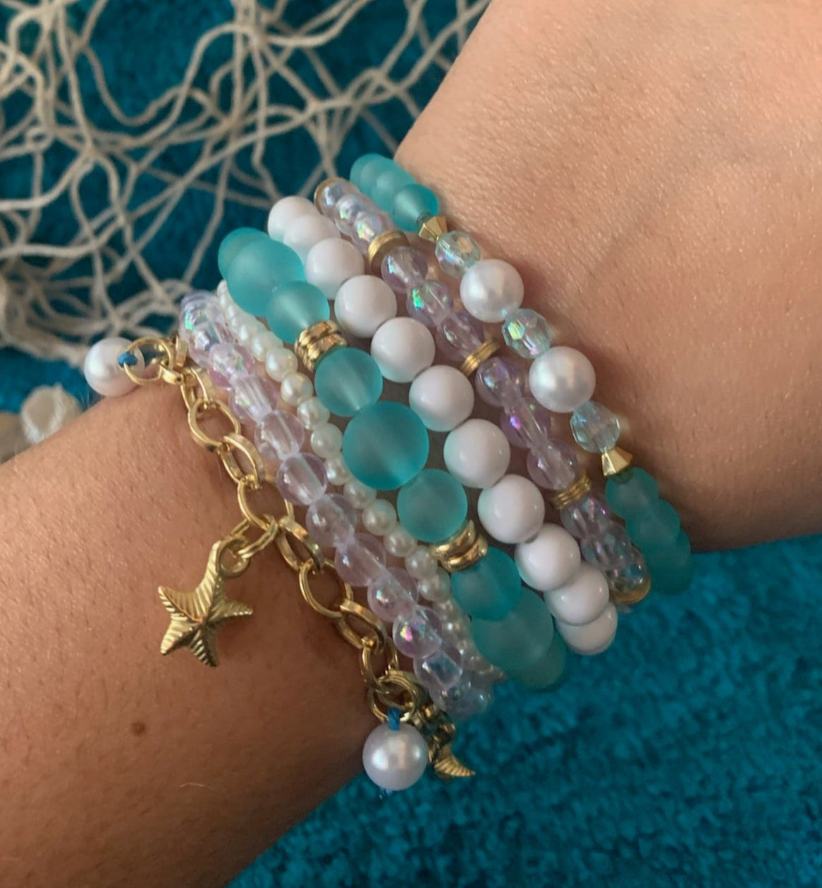 Beaded bracelets with a gold charm on a wrist against a textured blue background