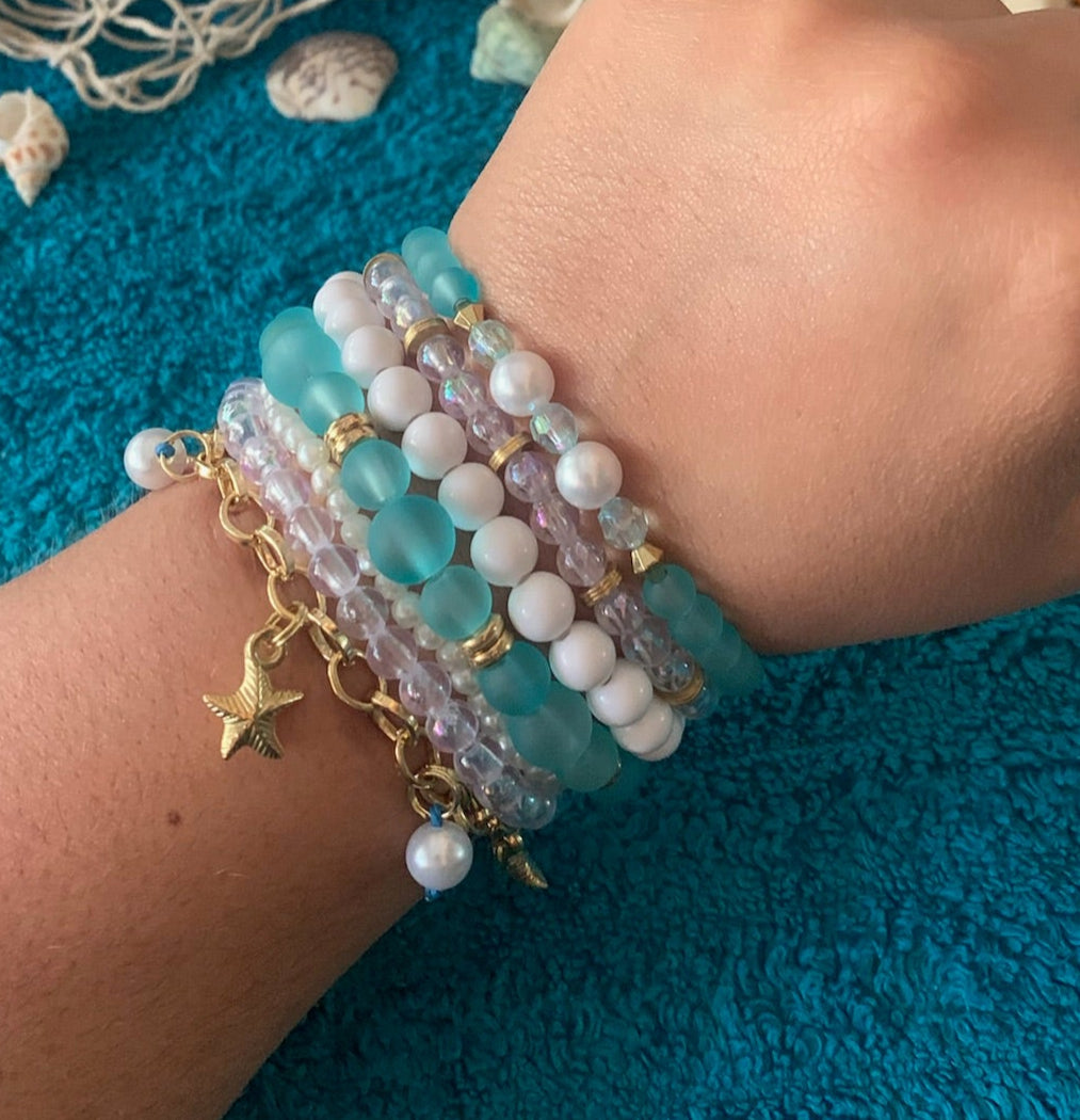 Hand wearing multiple bracelets on a textured blue surface with fishing net in background