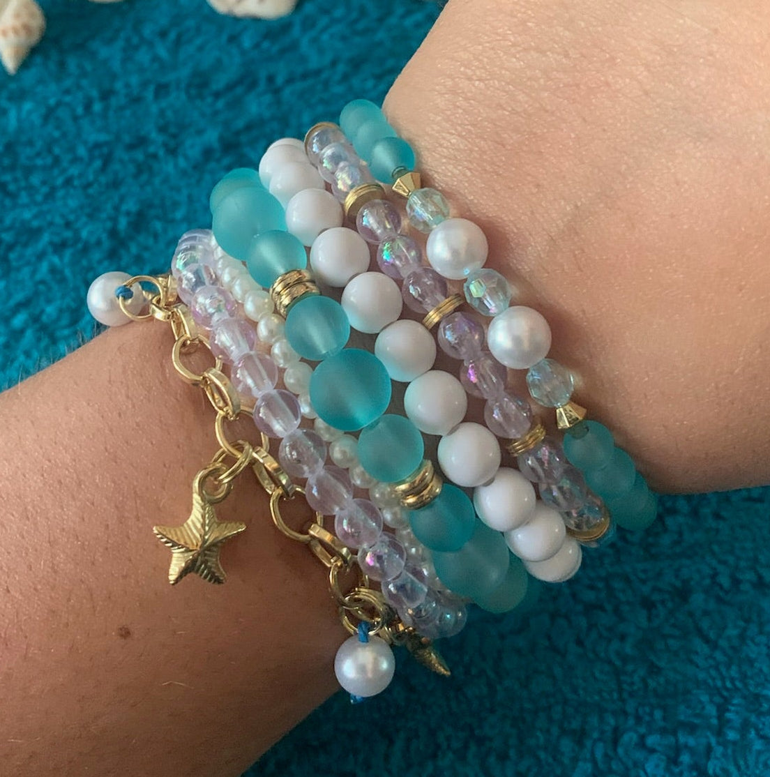 Close-up of a wrist wearing multiple beaded bracelets with a textured blue background