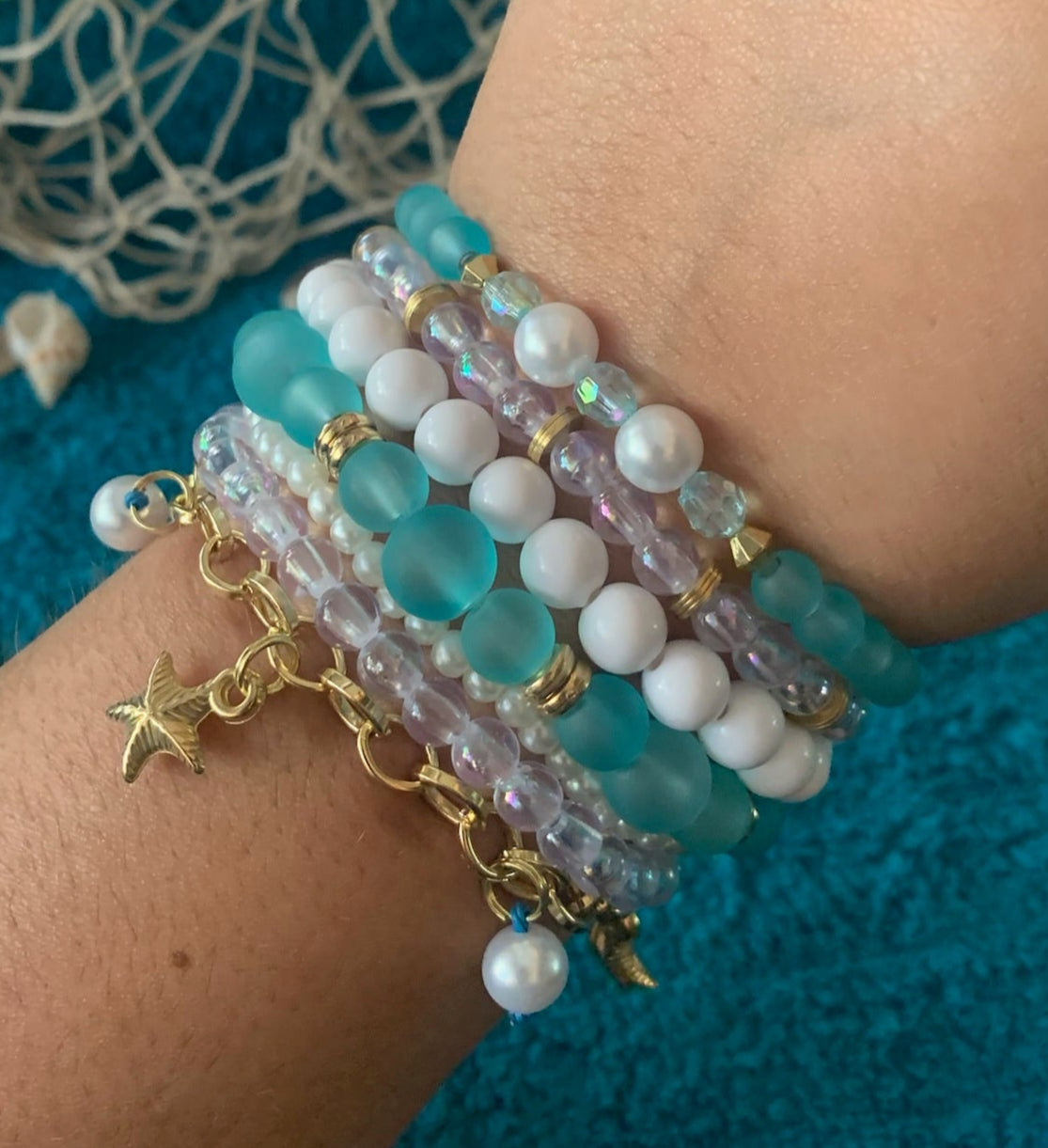 Wrist wearing multiple beaded bracelets with a textured blue background