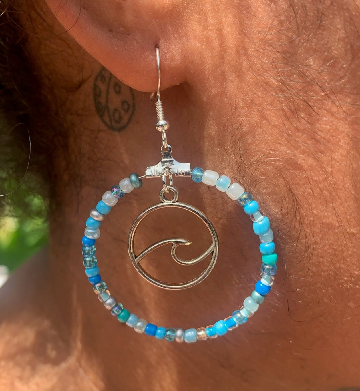 Close-up of an ear wearing a beaded hoop earring with a wave design.