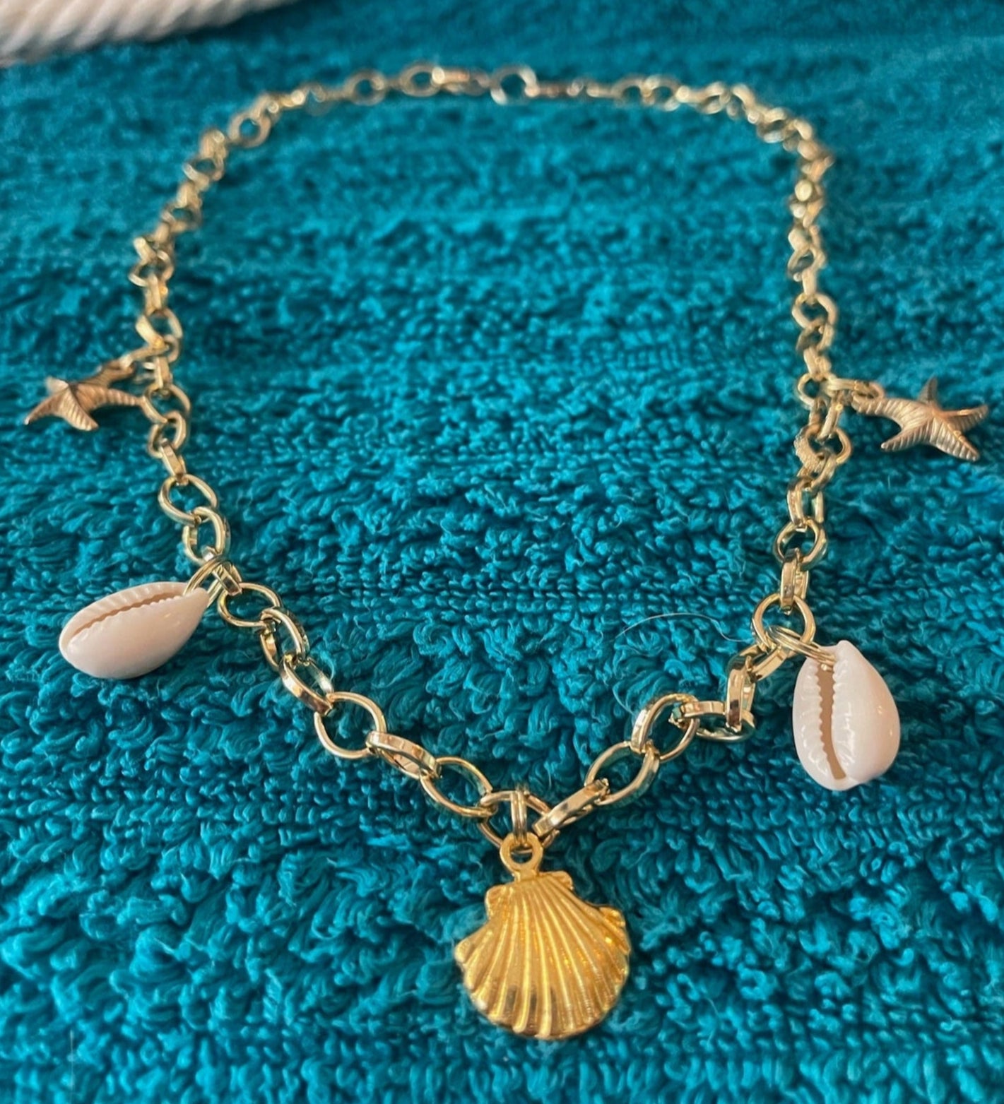 Gold bracelet with shell and star charms on a blue textured fabric background
