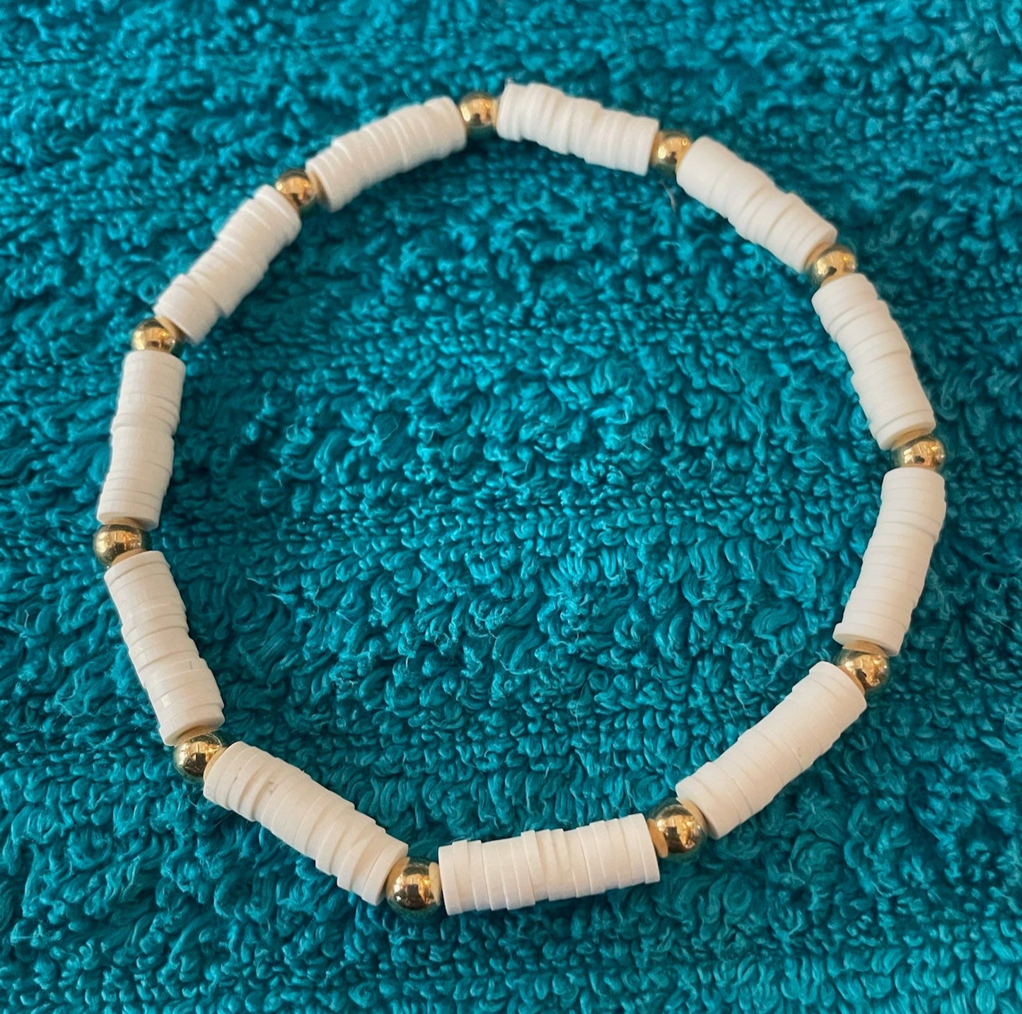 White beaded bracelet with gold accents on a blue textured surface