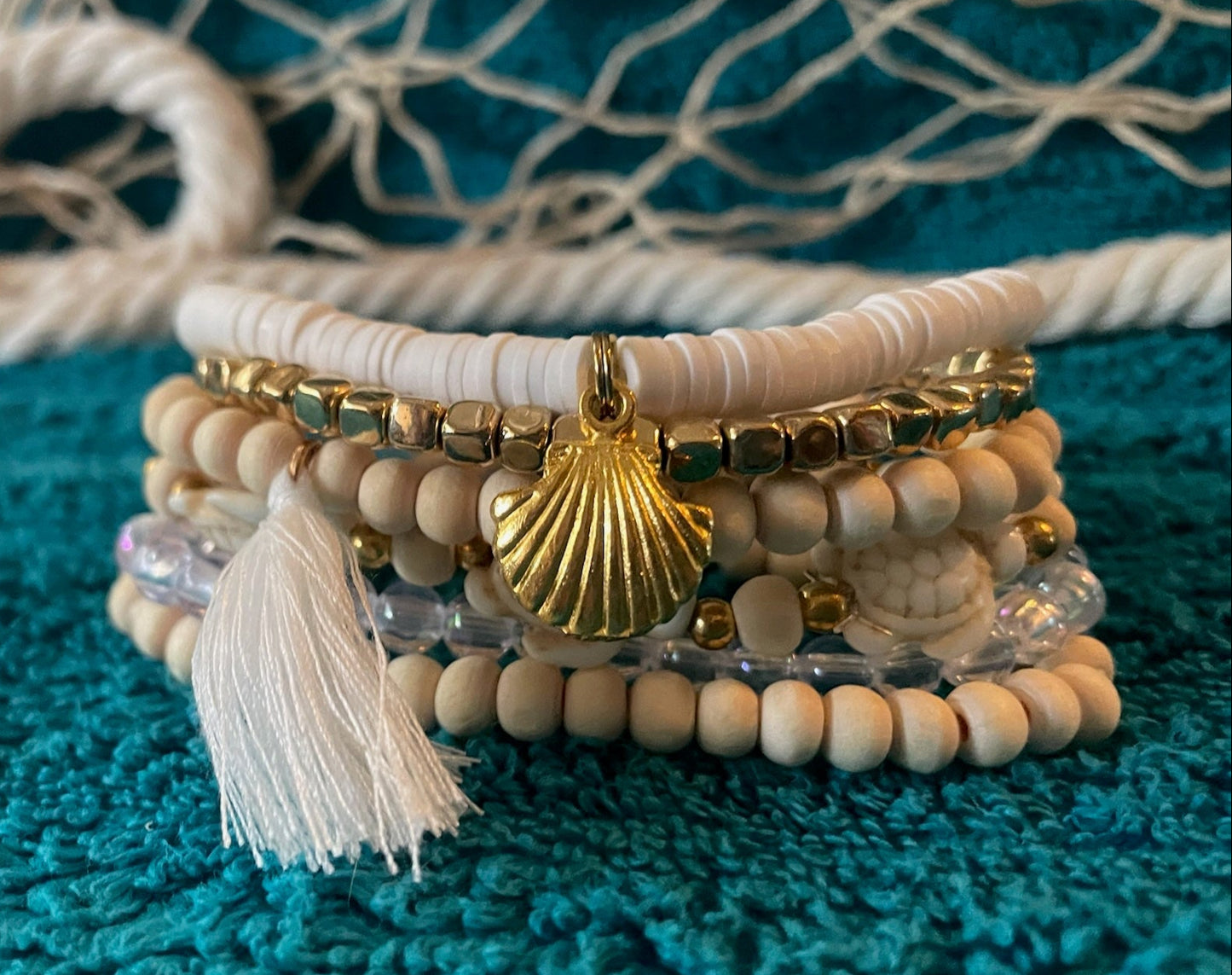 Stack of beaded bracelets with a shell charm on a textured blue surface