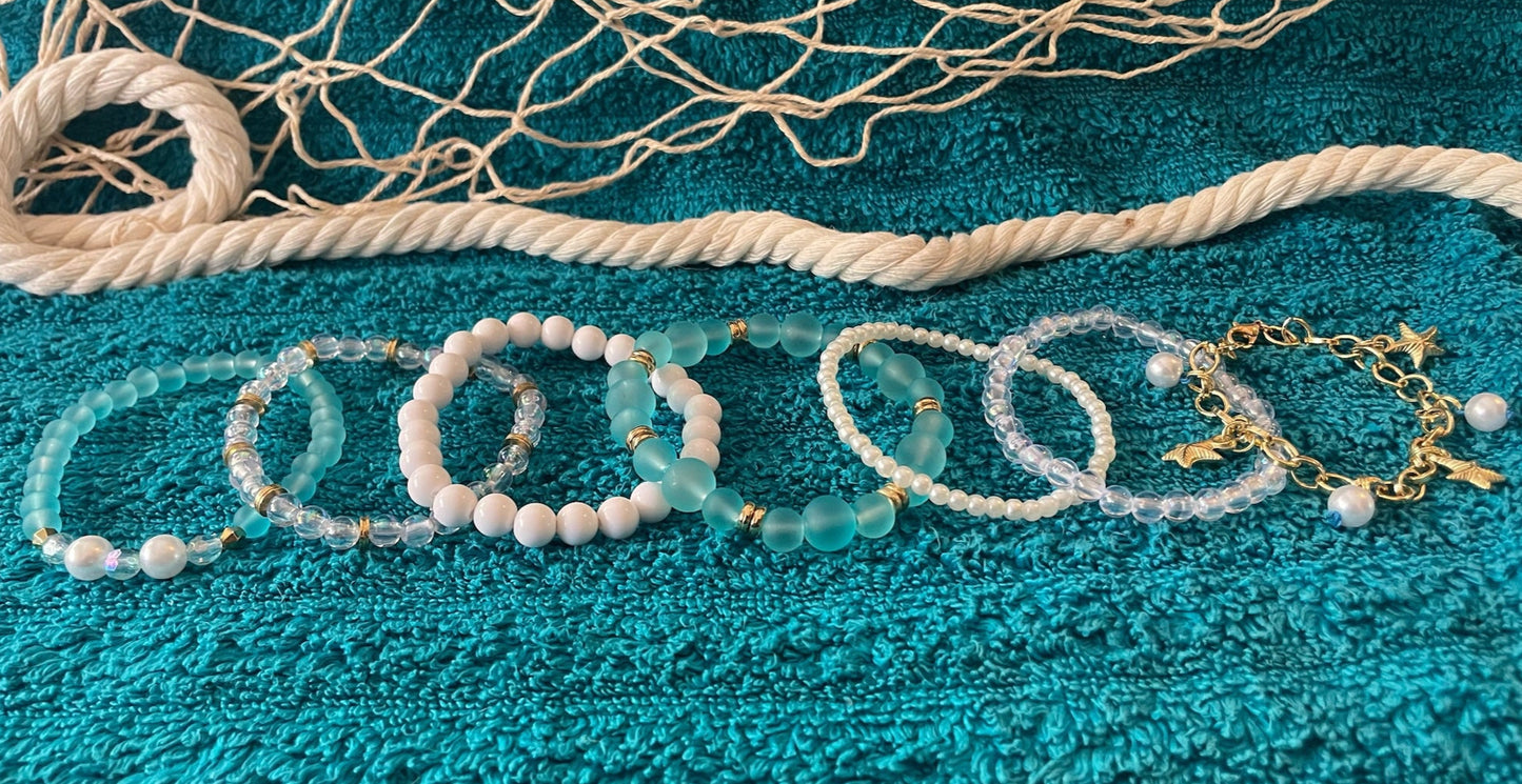 Jewelry set including bracelets and necklaces on a textured teal surface with fishing net.