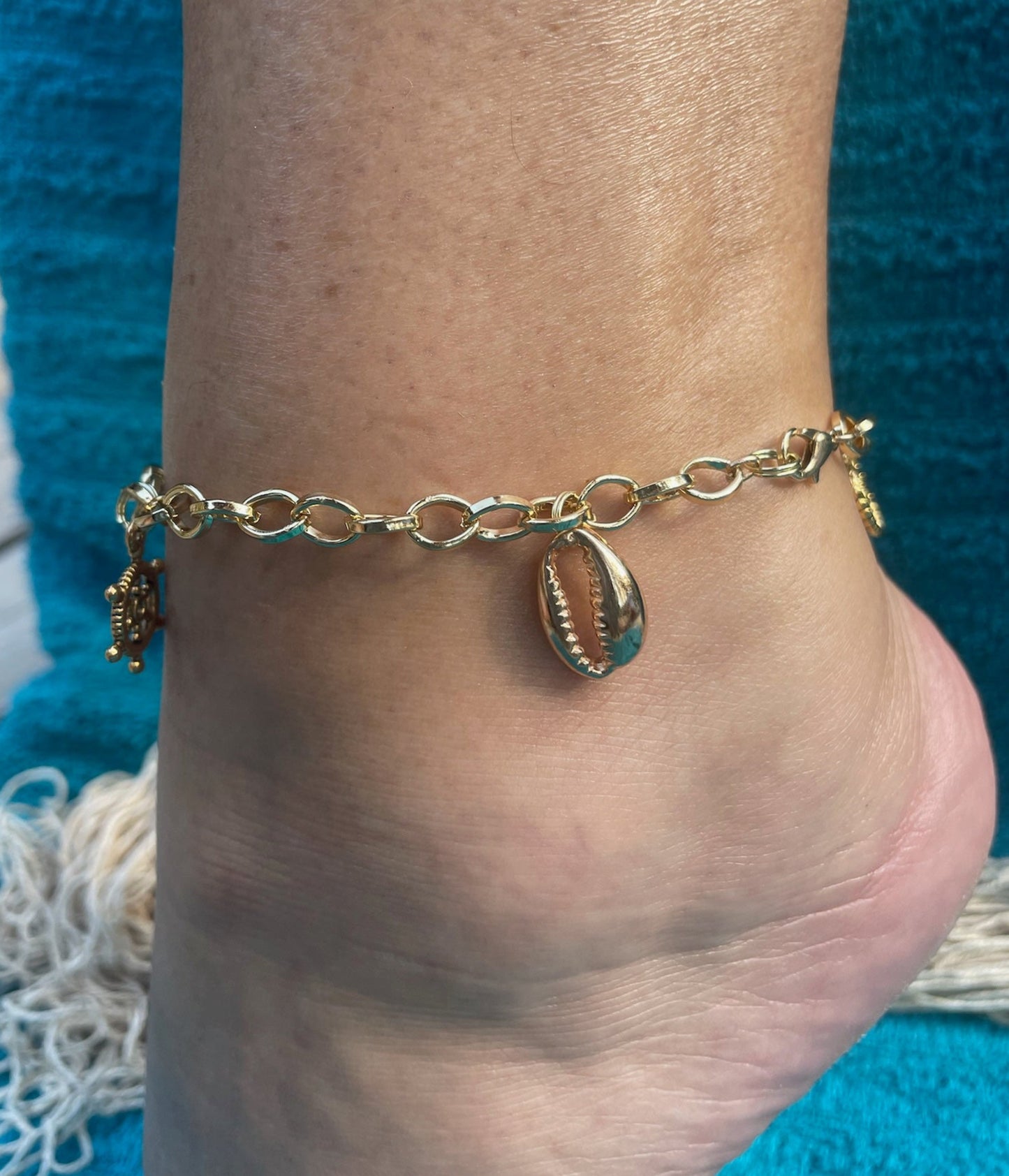 Gold anklet with shell charm on a foot against a blue fabric background