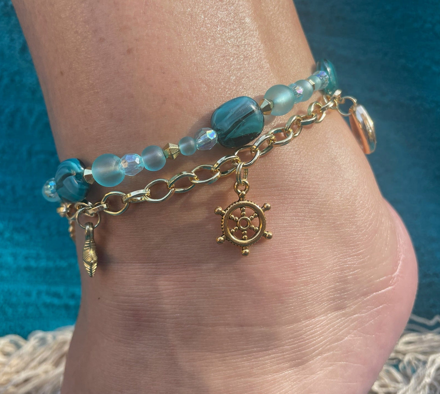 Ankle bracelet with blue beads and a gold charm on a foot against a blue background