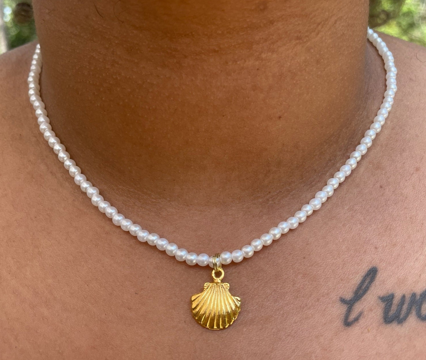 Pearl necklace with a gold shell pendant worn by a person outdoors.