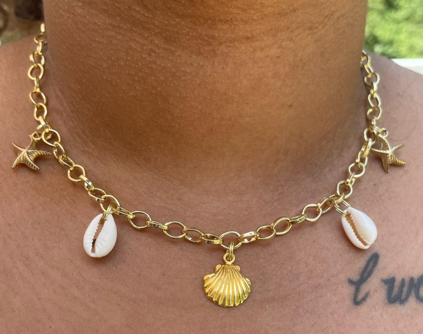 Gold necklace with shell and star charms worn by a person.