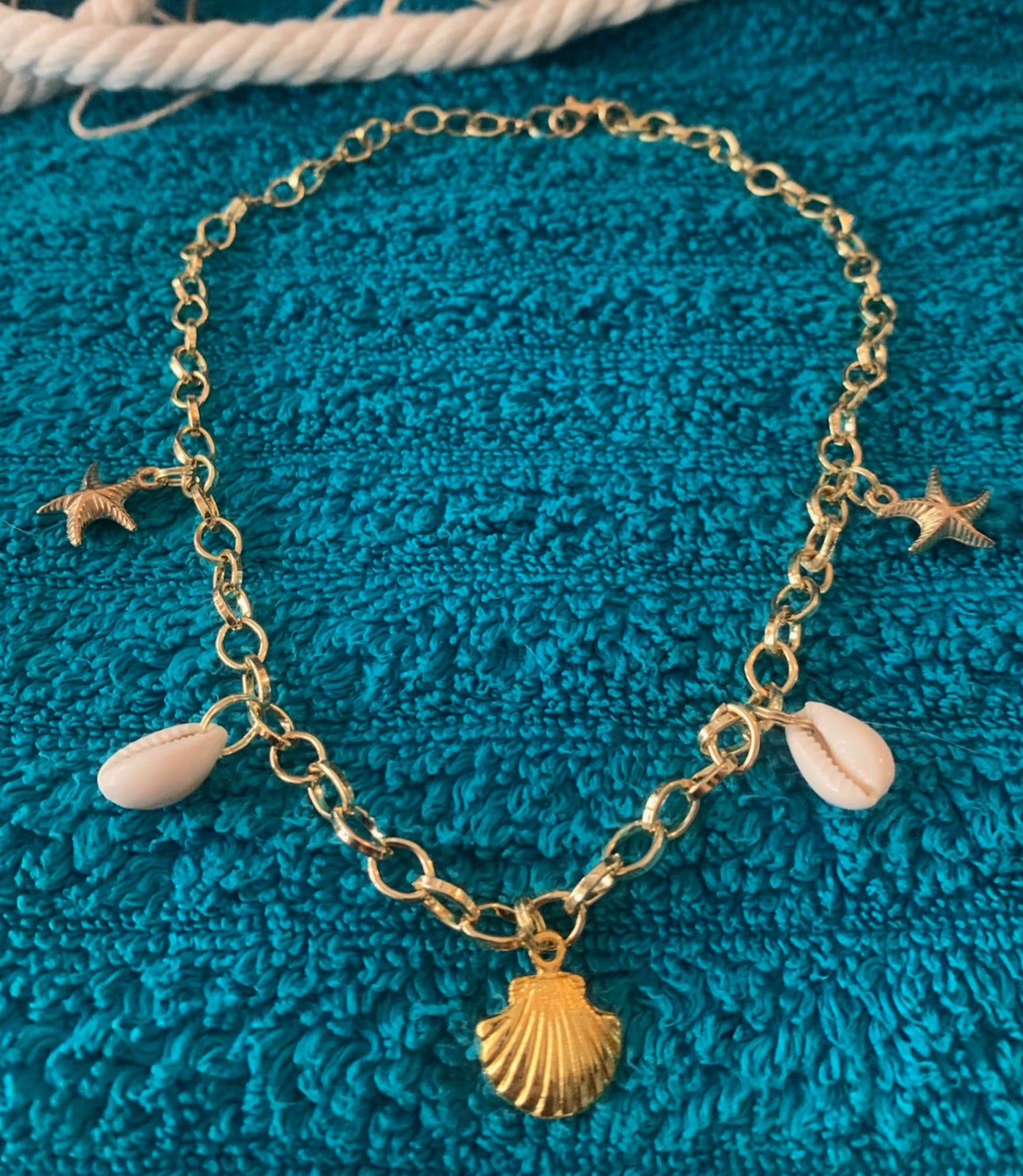 Gold bracelet with shell and starfish charms on a blue textured surface