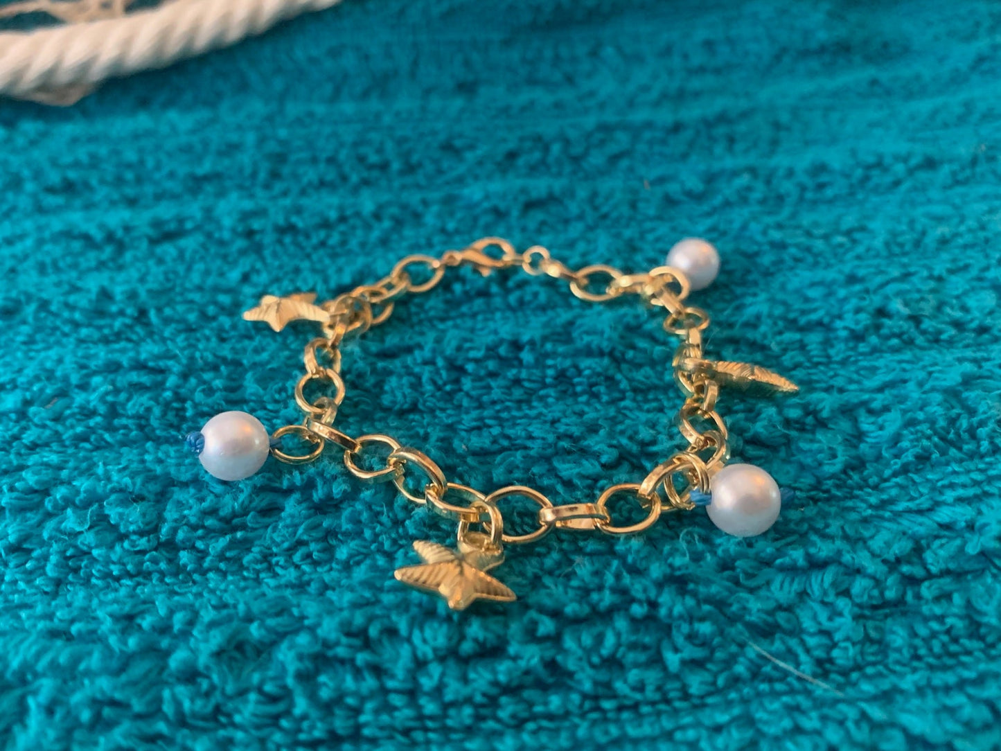 Gold bracelet with star and pearl charms on a blue textured fabric background