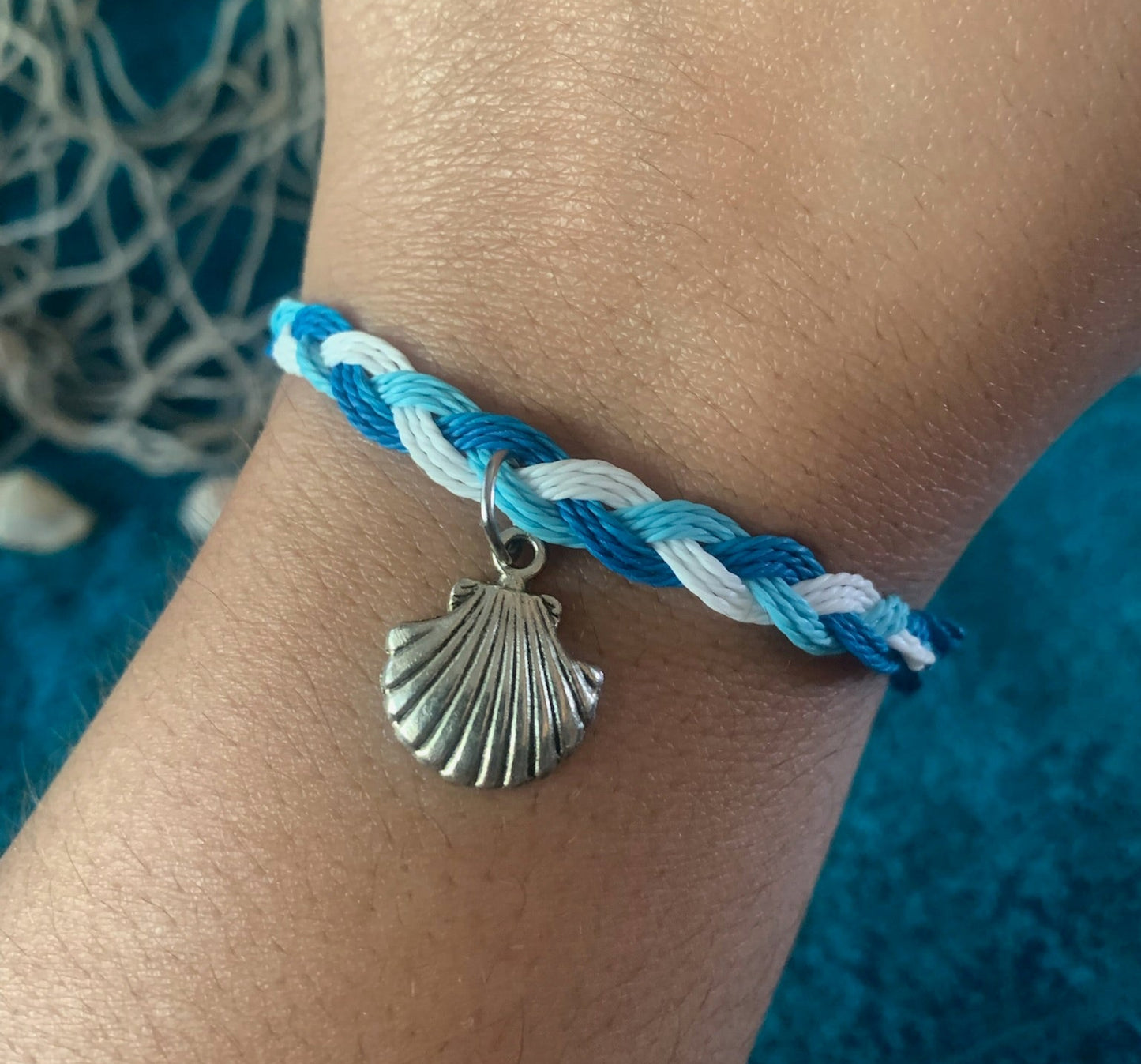 Bracelet with a shell charm on a wrist against a textured blue background