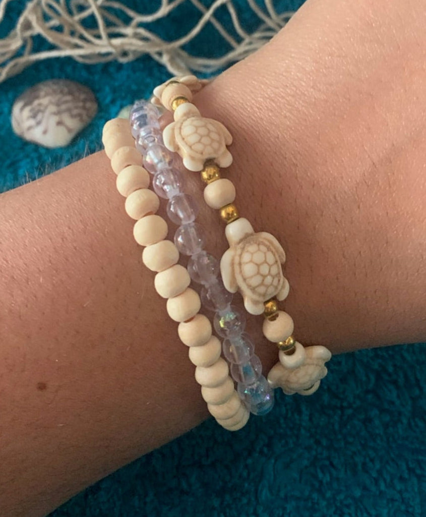 Close-up of a wrist wearing two bracelets on a textured blue surface with seashells.