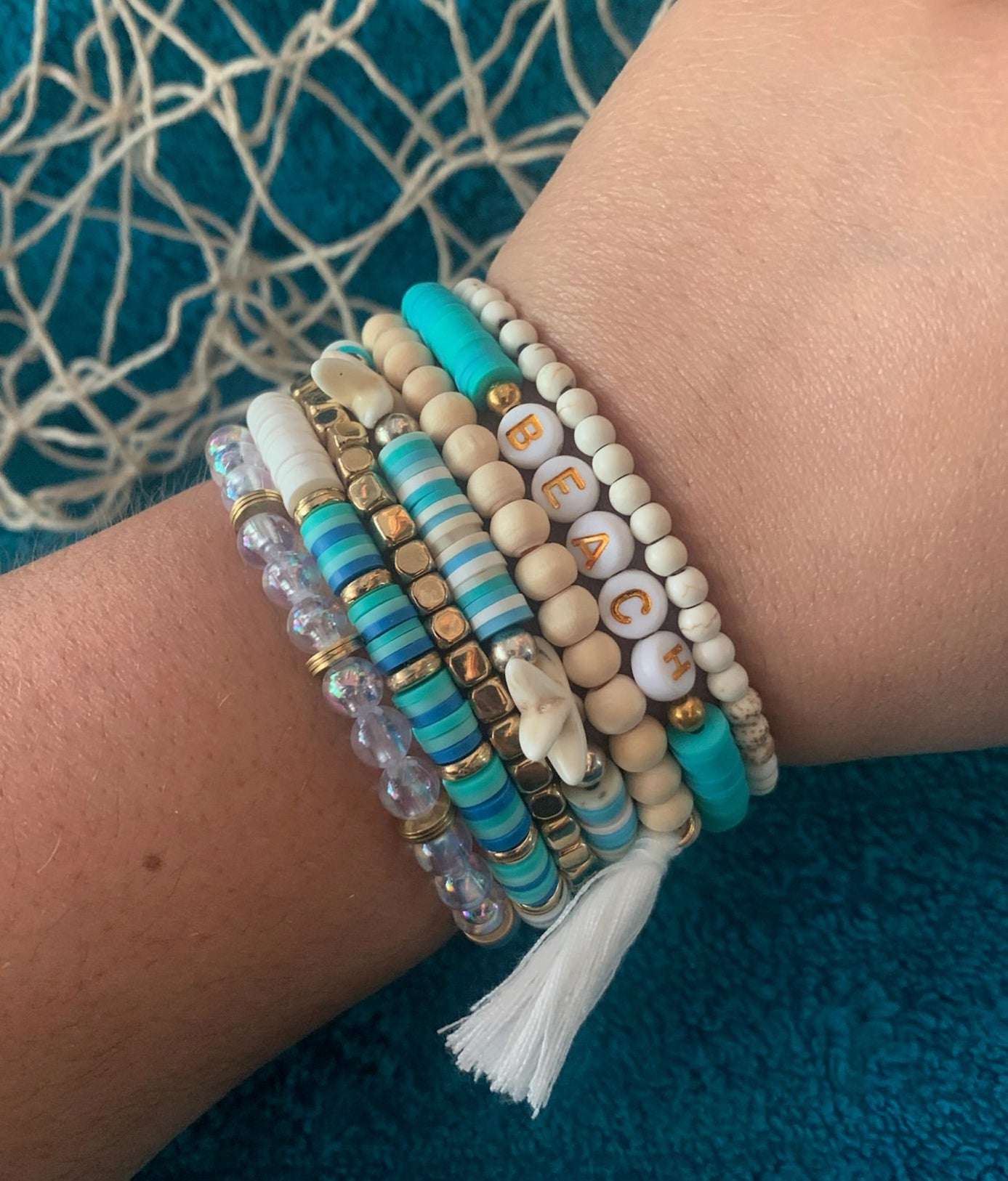 Close-up of a wrist wearing multiple beaded bracelets on a textured blue background