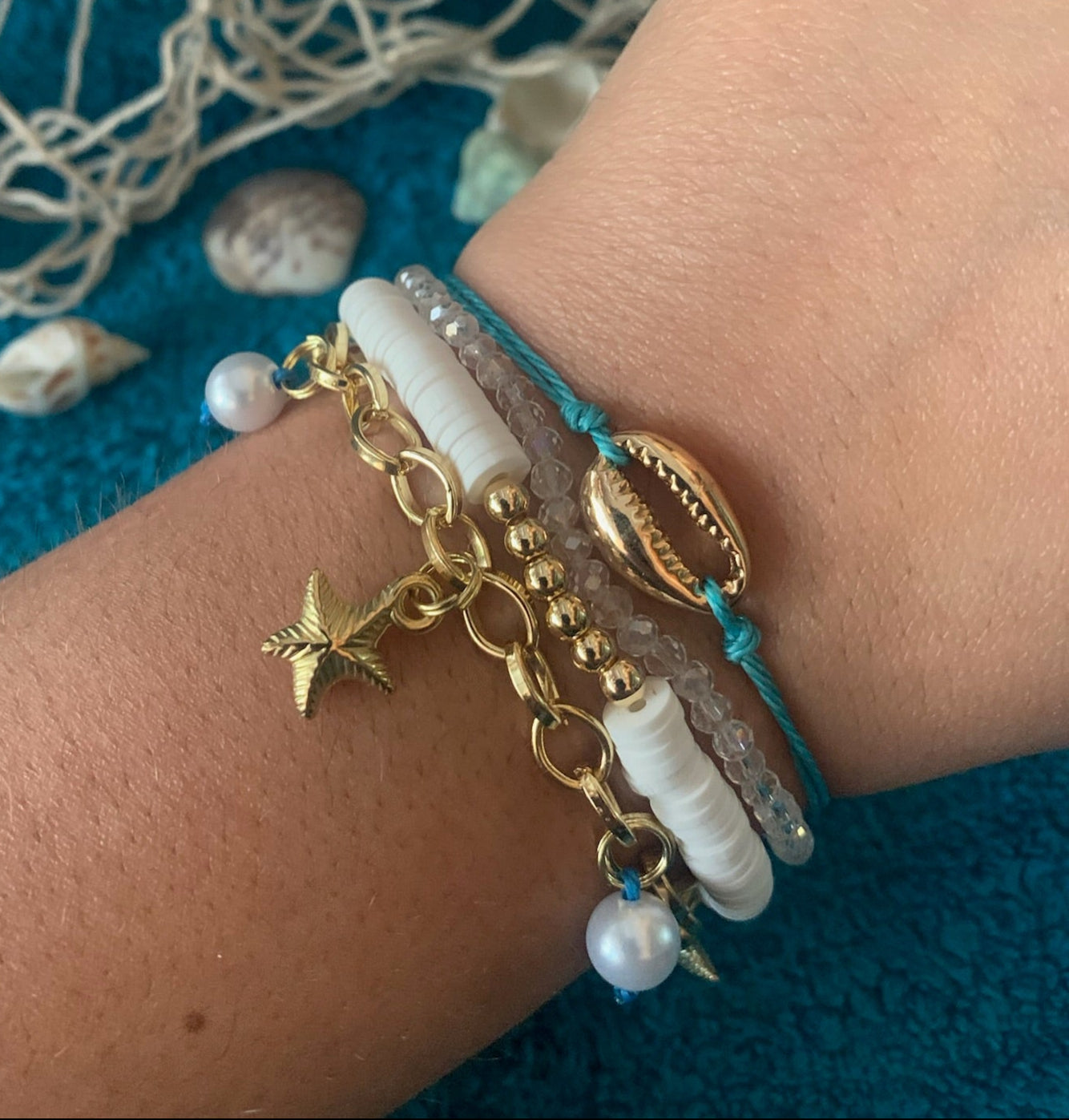 Bracelet with gold charms and pearls on a wrist against a textured blue background