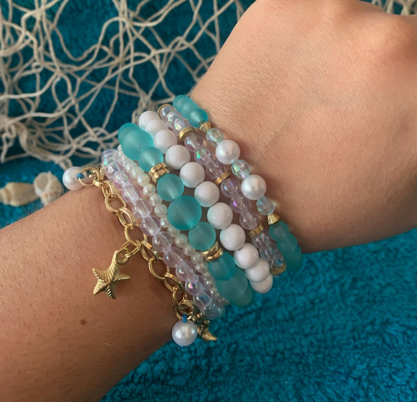 Hand wearing multiple beaded bracelets on a textured blue fabric background