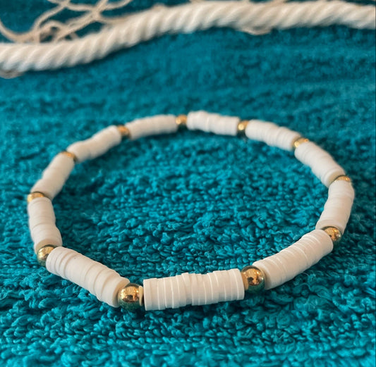 White beaded bracelet with gold accents on a blue textured surface