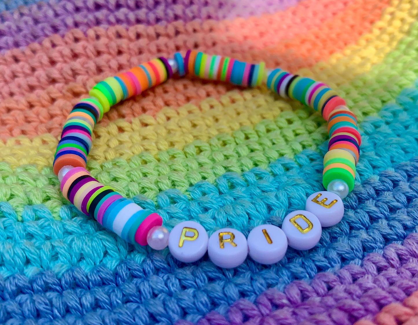 Colorful beaded bracelet with 'PRIDE' on a rainbow-patterned fabric background