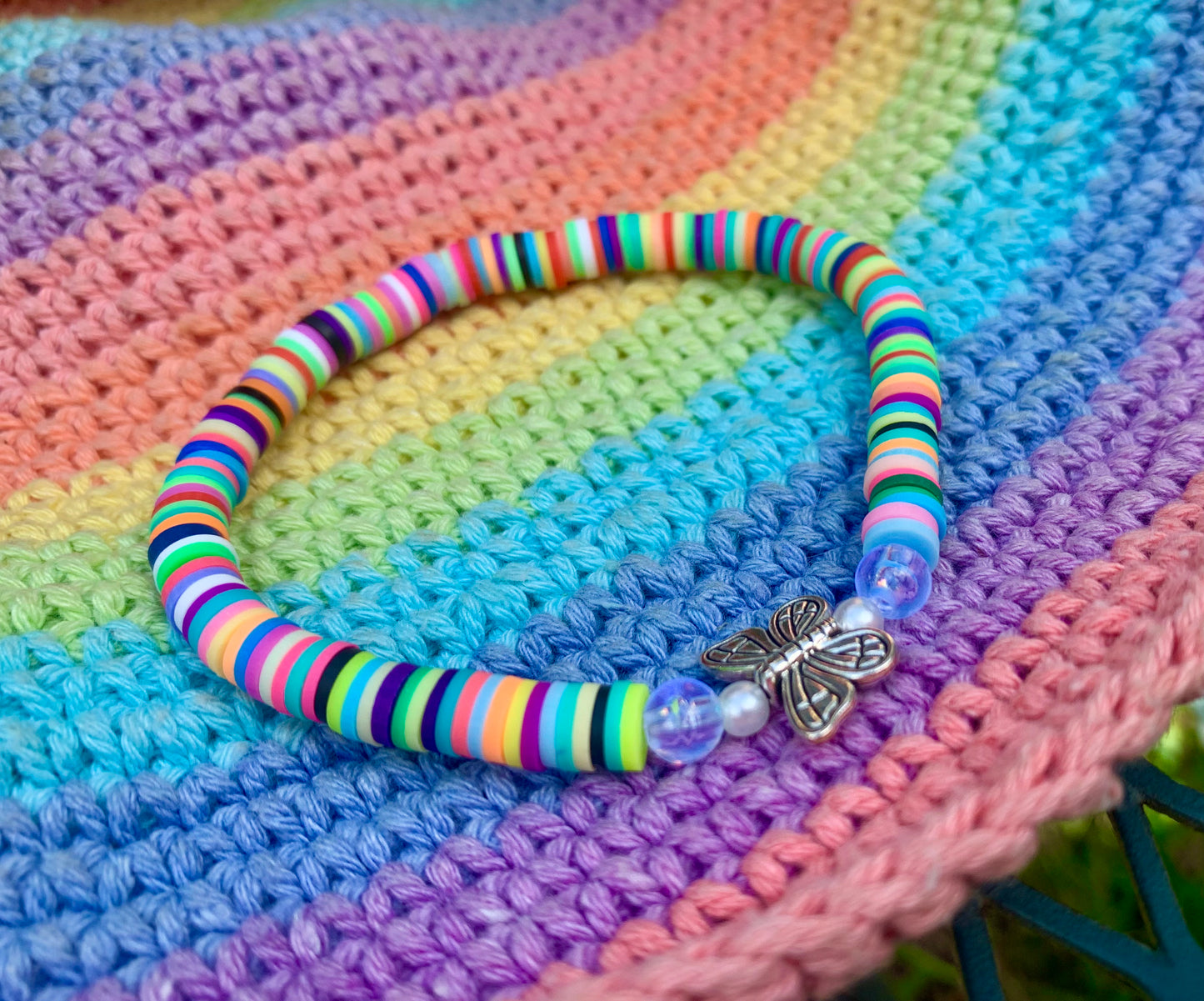 Colorful striped heishi bead bracelet with a silver butterfly charm on a multicolored crocheted surface.