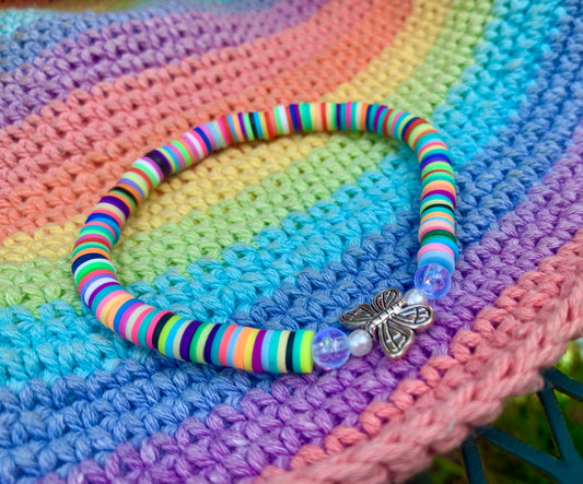 Colorful striped heishi bead bracelet with a silver butterfly charm on a multicolored crocheted surface.