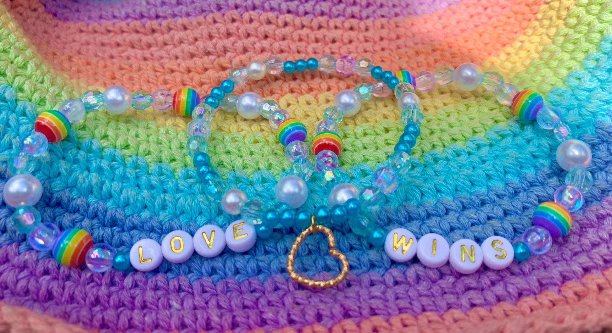 Colorful beaded bracelets with letter beads spelling "LOVE WINS" on a rainbow-patterned crocheted fabric background