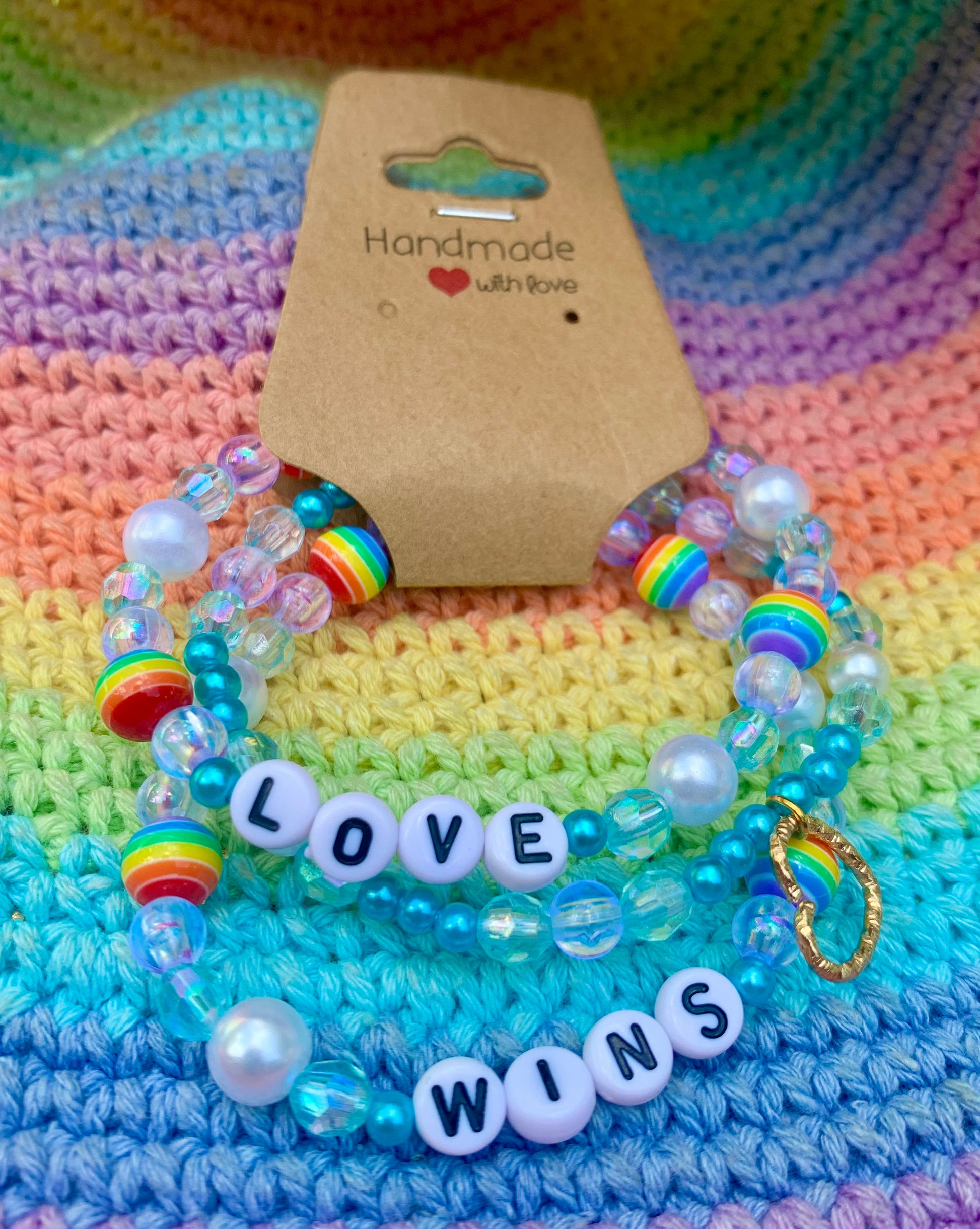 Set of colorful beaded bracelets with 'LOVE WINS' message on a rainbow-patterned fabric background.