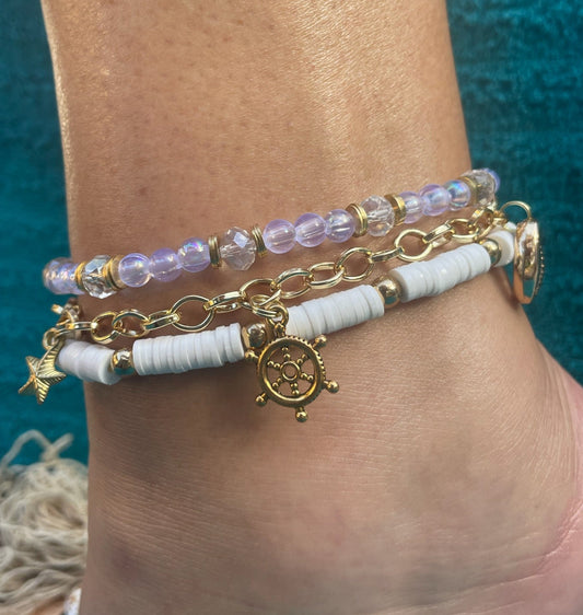 Close-up of a person's ankle wearing multiple bracelets with charms against a blue background.