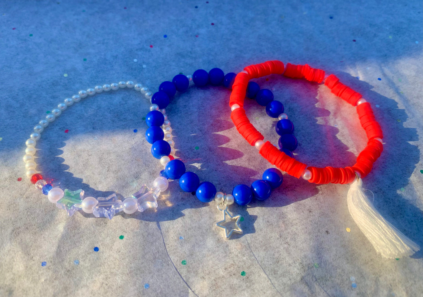 Three beaded bracelets in red, blue, and clear on a textured surface.