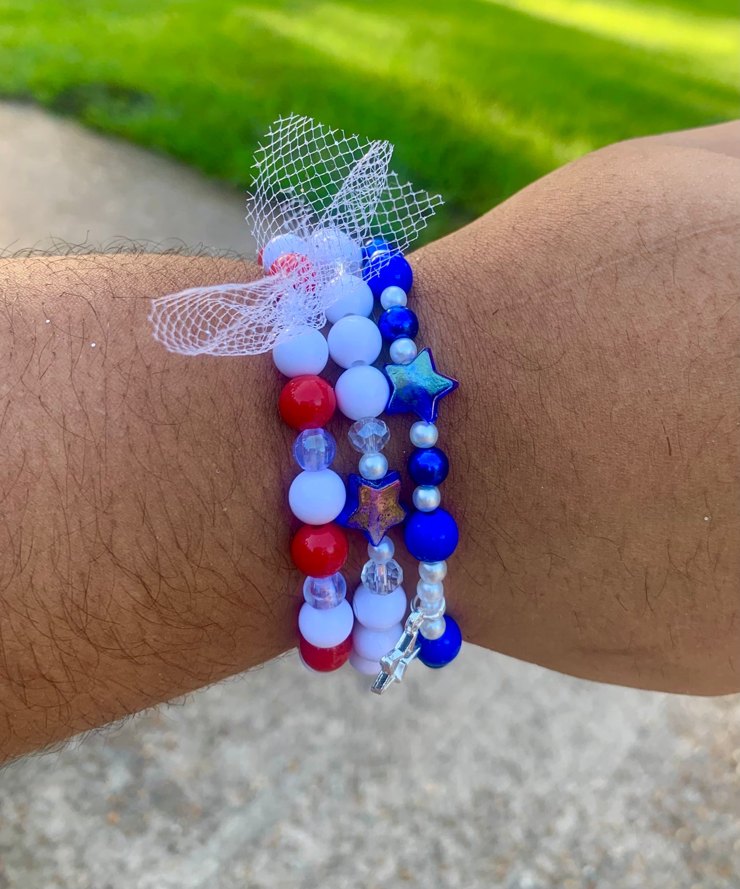 Beaded bracelet with red, white, and blue beads on a wrist against a blurred natural background