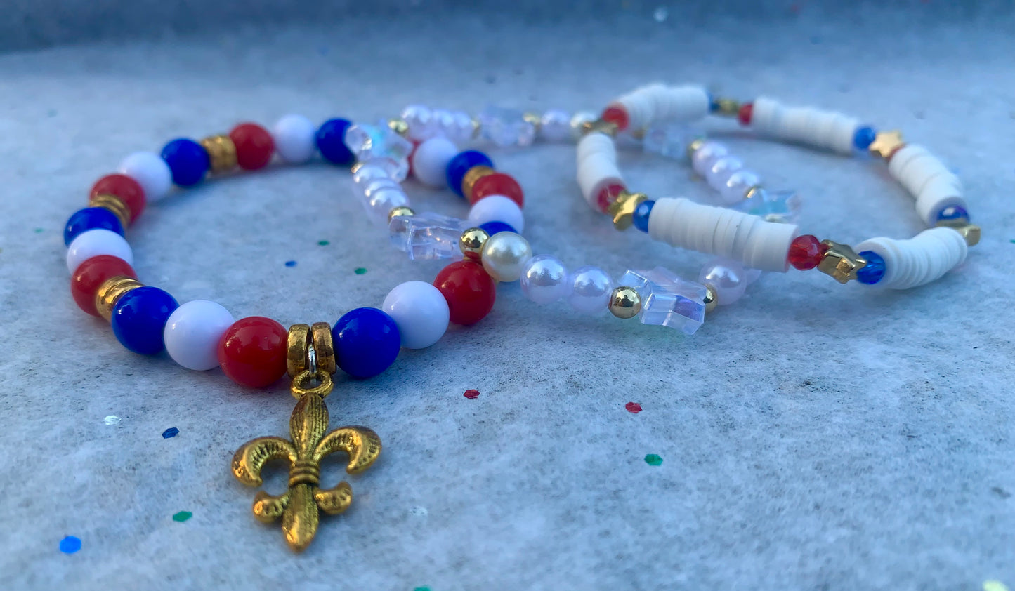 Colorful beaded bracelets with a gold fleur-de-lis charm on a textured surface.