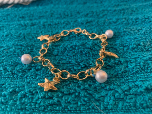 Gold bracelet with starfish and pearl charms on a teal fabric background