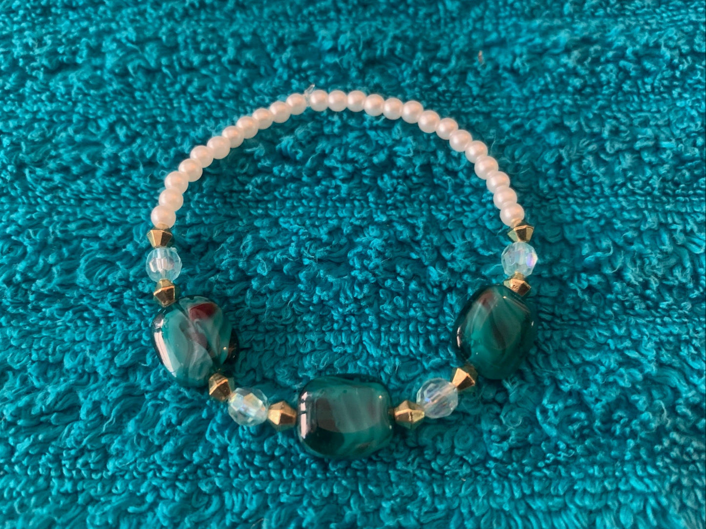Beaded bracelet with green and clear beads on a textured blue surface