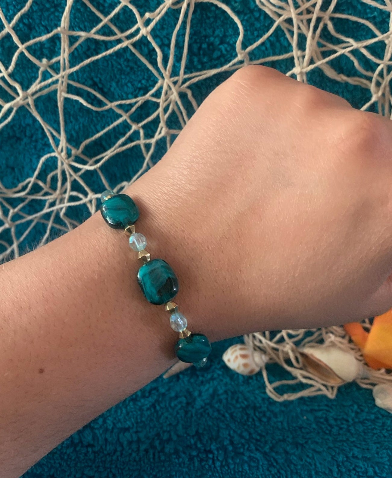 Hand wearing a blue beaded bracelet on a textured blue fabric background