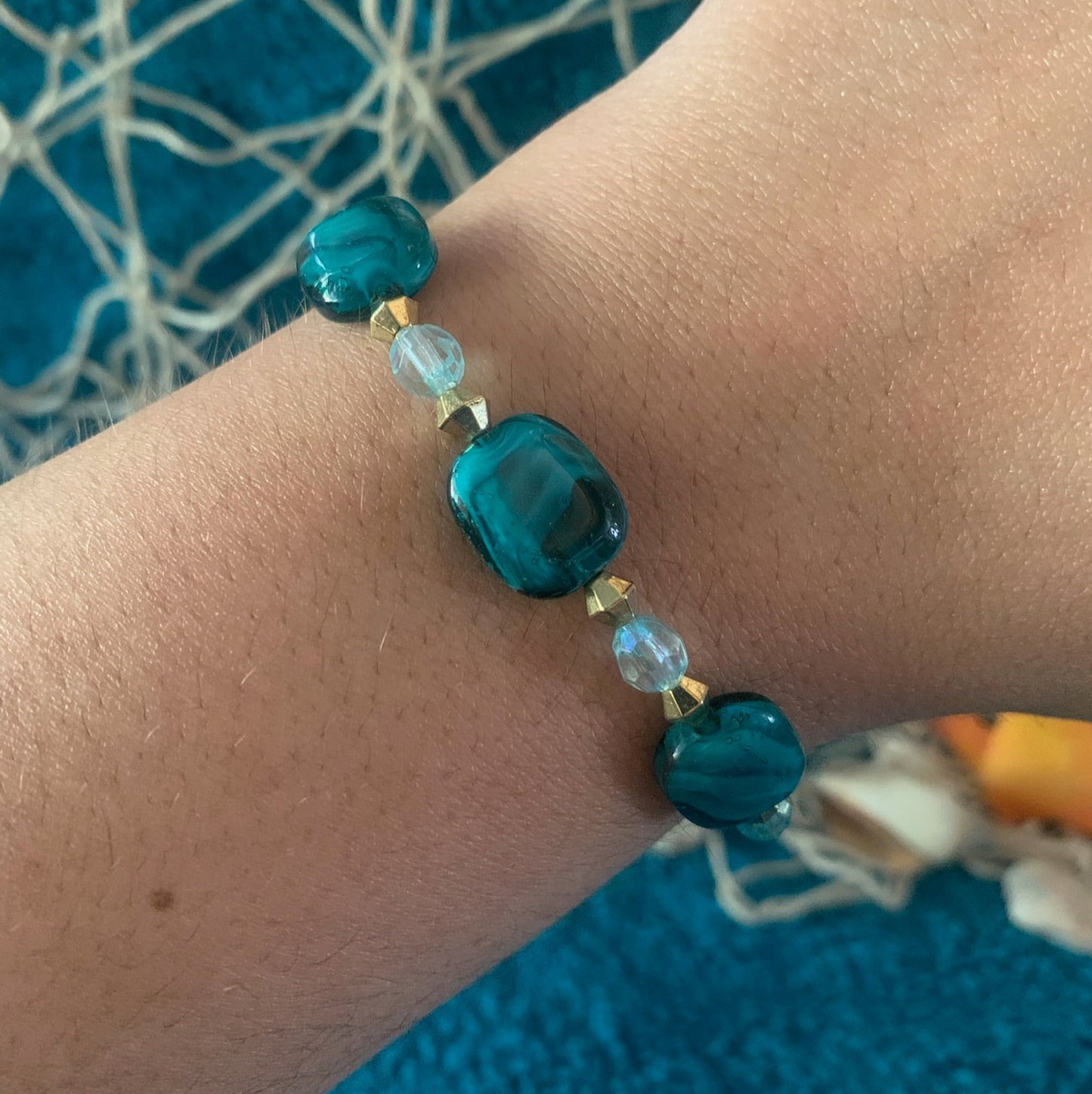 Teal beaded bracelet on a wrist with a blue textured background