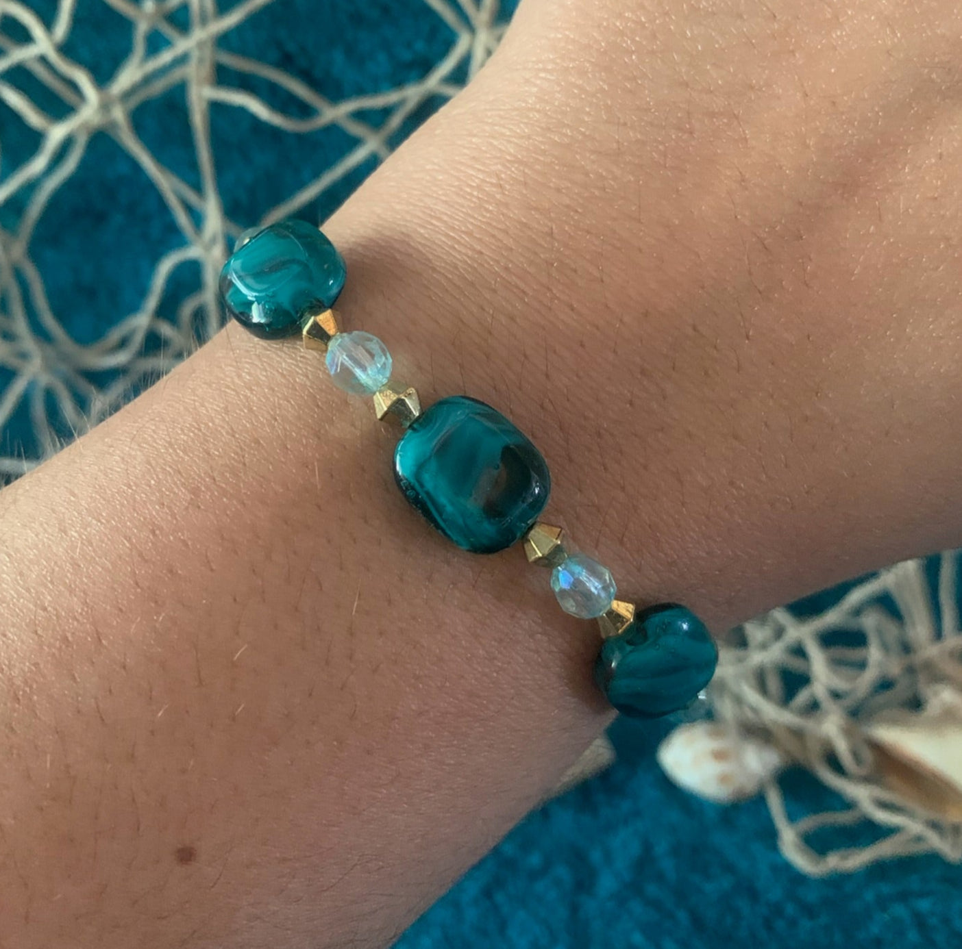 Teal beaded bracelet on a wrist with a blue textured background