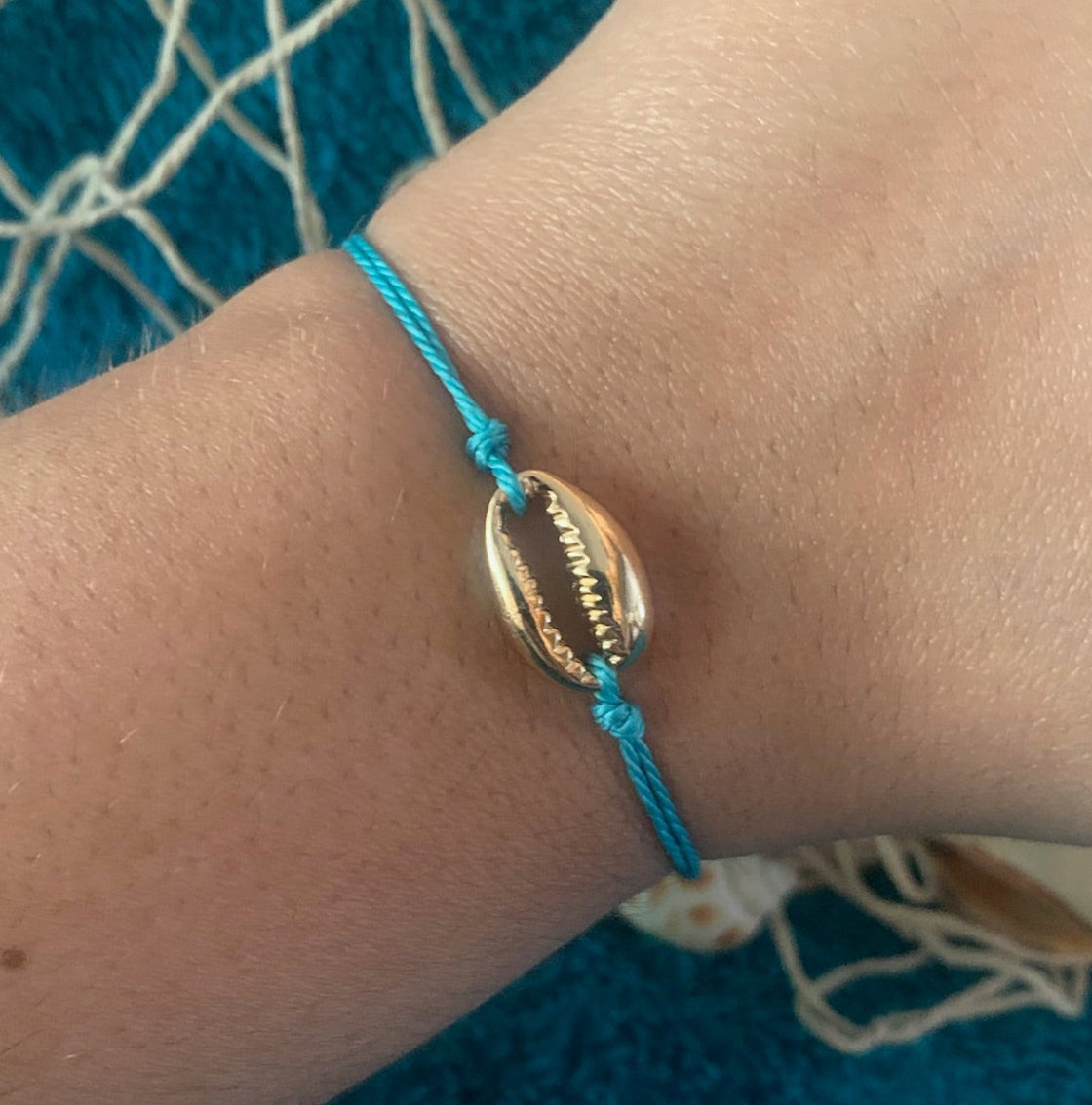Hand wearing a blue bracelet with a gold bead against a textured blue background