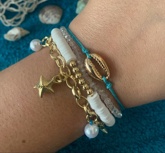 Bracelet with gold chain, star charm, and white beads on a wrist against a textured blue background.